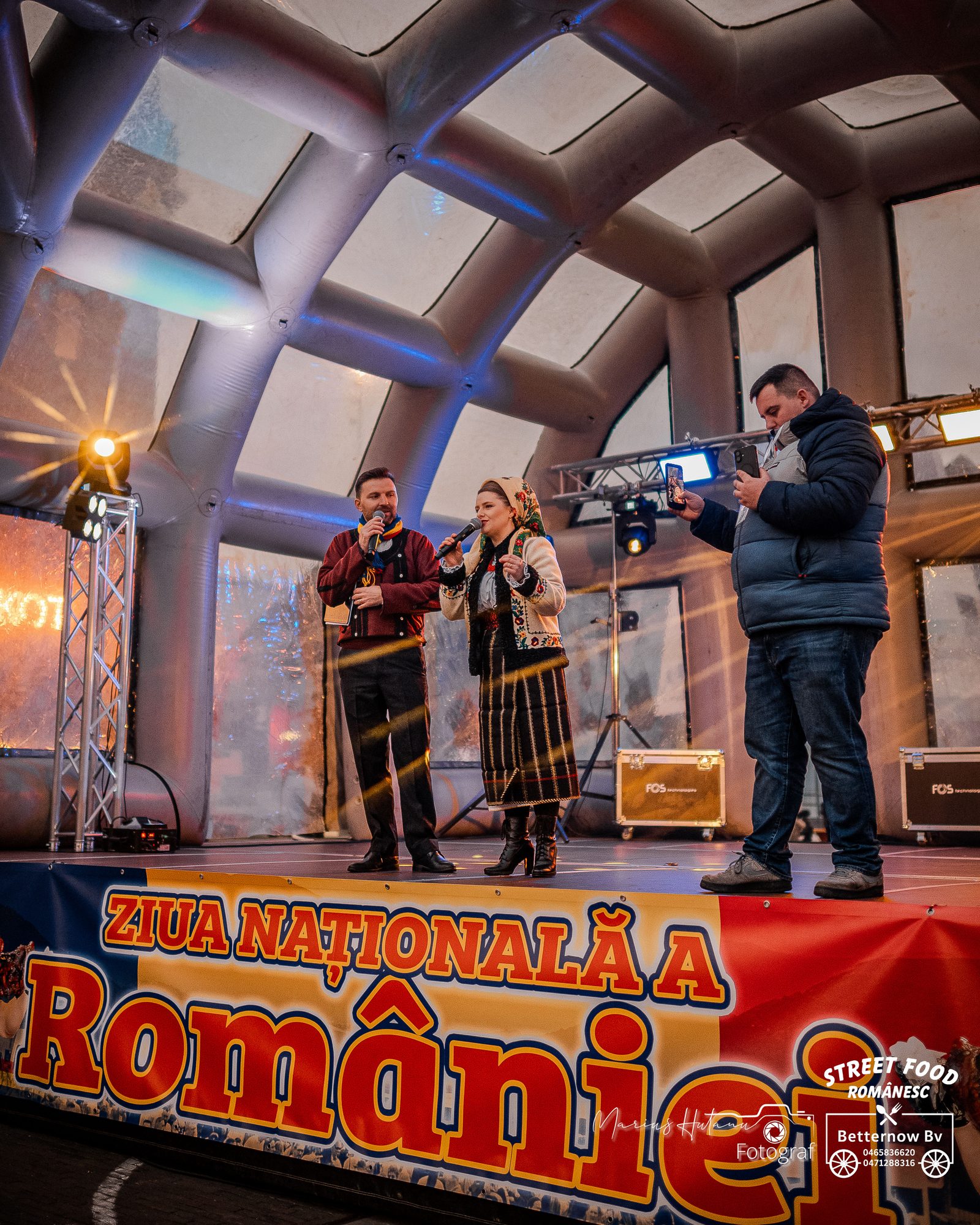 Presenters speaking on a community event stage at night.